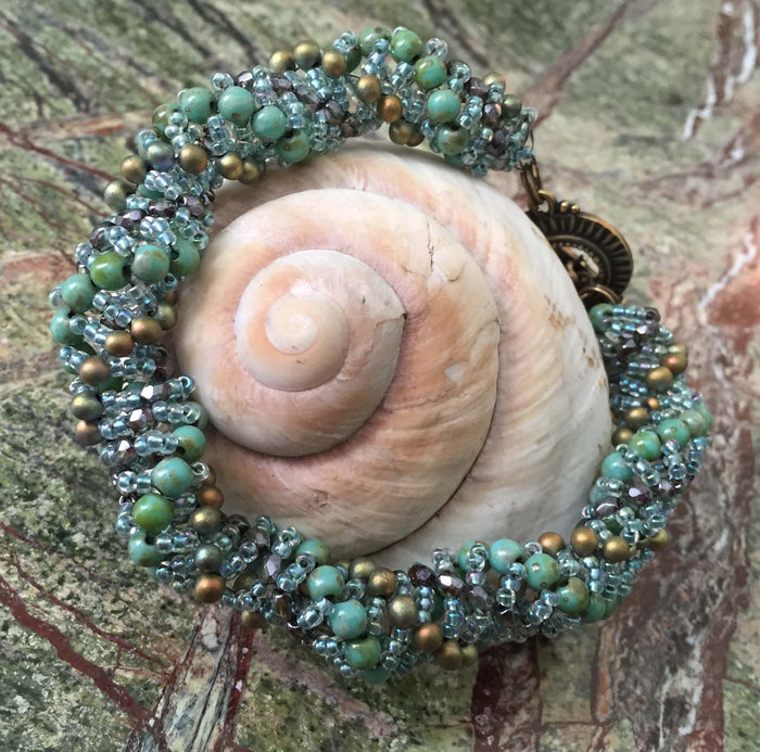 Dutch Spiral beaded bracelet pattern using Czech Fire-polished glass, Czech druks, and seed beads in Turquuoise Green, pale clear blue and Bronze. This bracelet measures between 8 1/4" and 8 1/2"