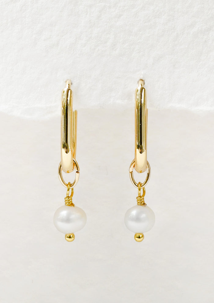 A pair of gold oval hoop earrings with a dangling freshwater pearl charm.