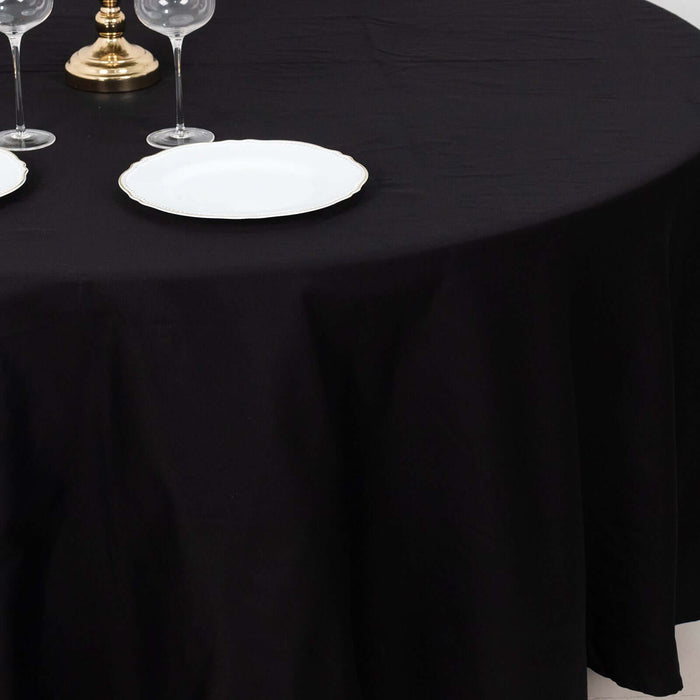 Black tablecloth with elegant white plates and glassware set for dining.