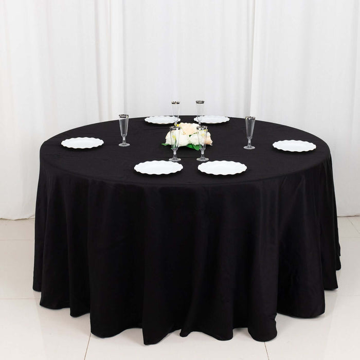 Round black table with white plates, elegant centerpiece, and glassware.