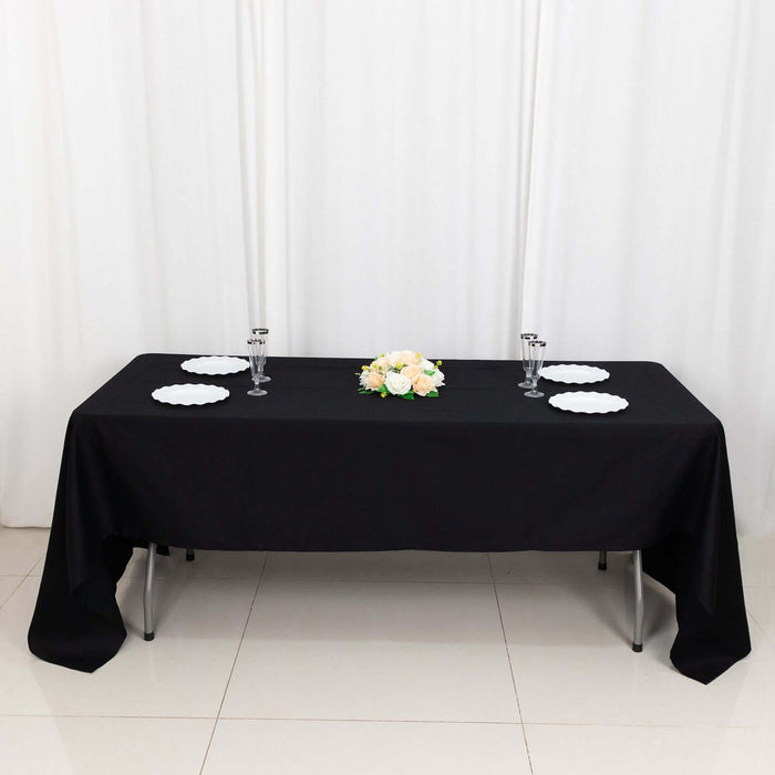 Black tablecloth with white plates and floral centerpiece on a table.