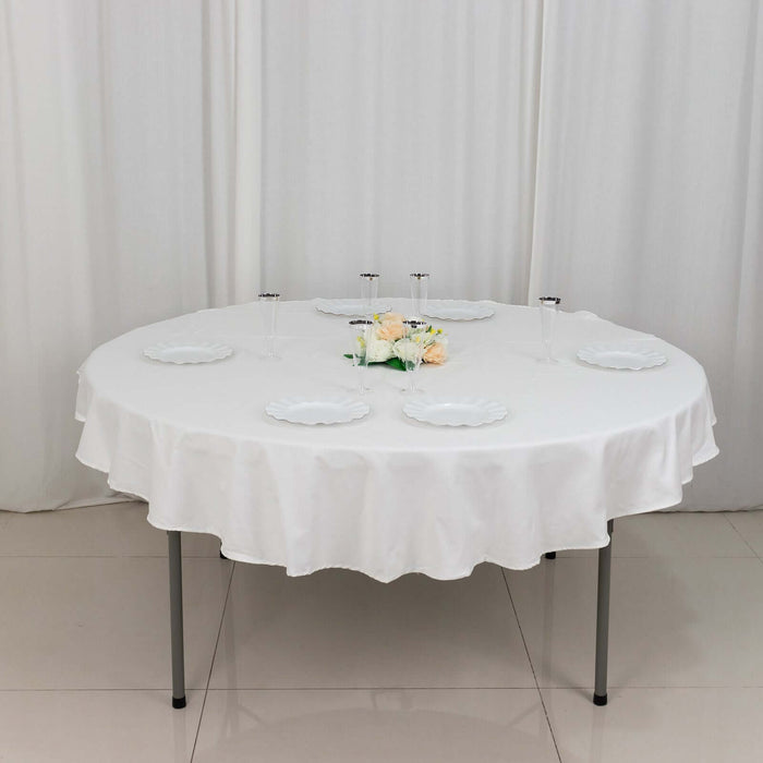Round table set with white tablecloth and plates, adorned with flowers.