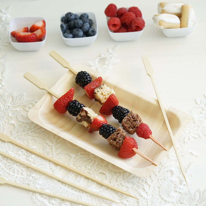 Fruit and granola skewers on a wooden plate with fresh berries in bowls.