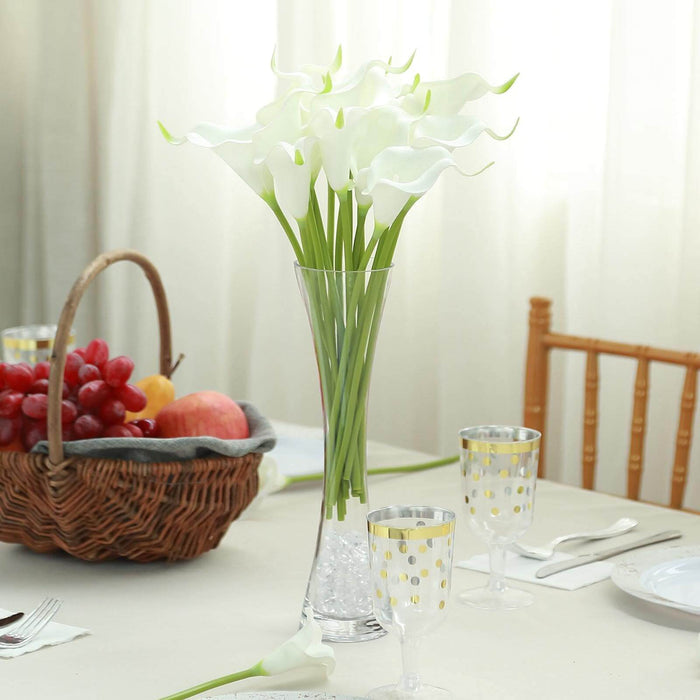 Elegant white calla lily arrangement in a tall glass vase on a dining table.