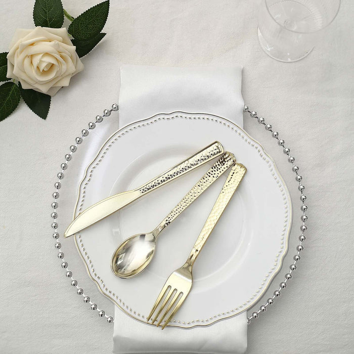 Elegant gold cutlery set on a decorative plate with a white napkin and rose.