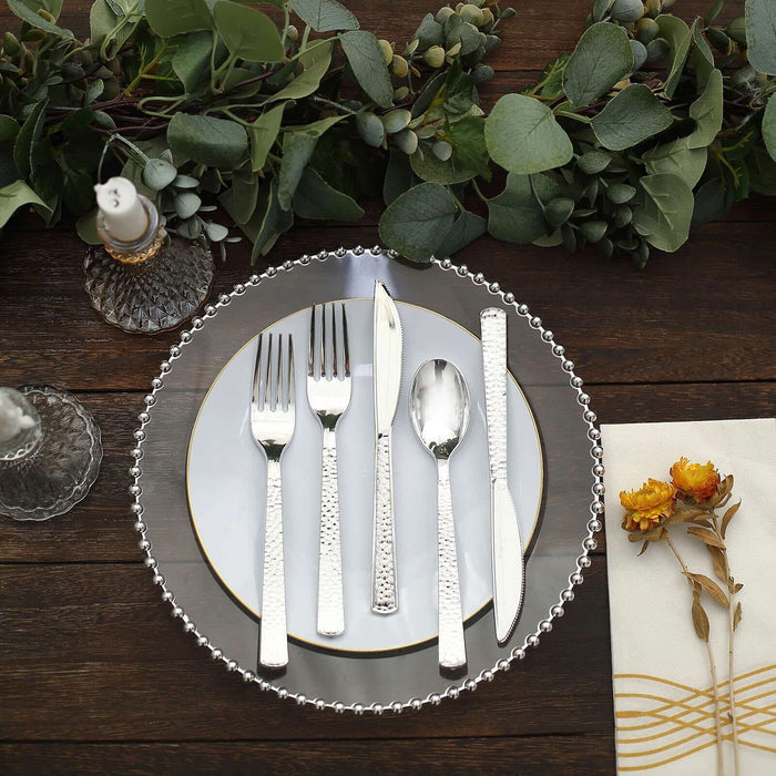 Elegant silver cutlery set arranged on a decorative plate with greenery backdrop.