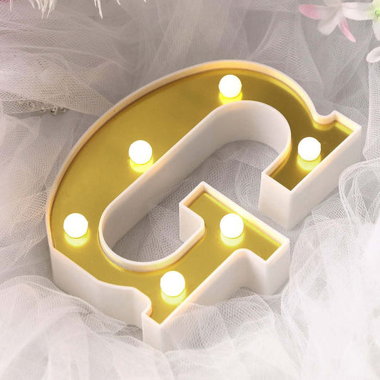 Gold and white marquee letter "G" with lights on a soft background.