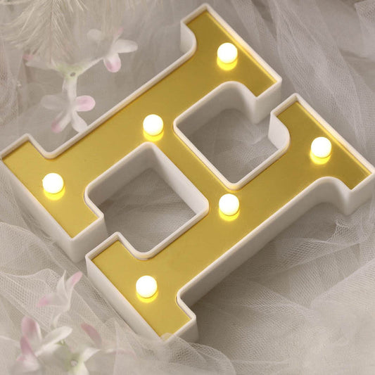 Decorative illuminated letter "H" in gold and white with lights.