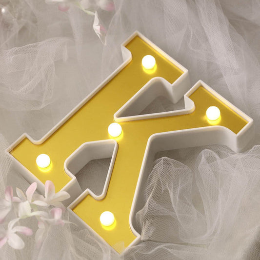 Yellow illuminated letter "K" on soft white fabric.