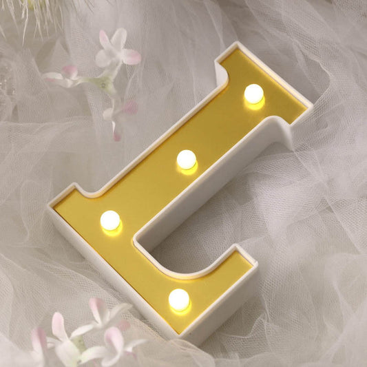 Yellow lit letter "L" decorative sign on soft white background.