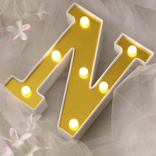 Illuminated yellow letter "N" with white lights on a soft fabric background.