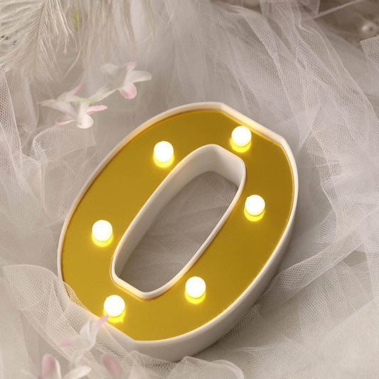 Yellow marquee letter "O" with lights on a soft fabric backdrop.