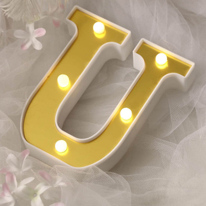 Decorative illuminated letter "U" with a gold background on soft fabric.