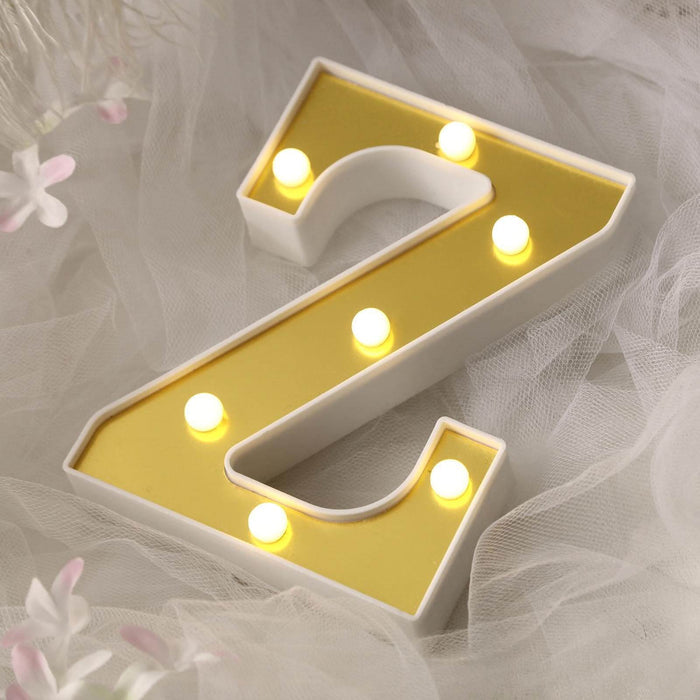 Lighted marquee letter "Z" in white and gold with bulbs, styled on soft fabric.