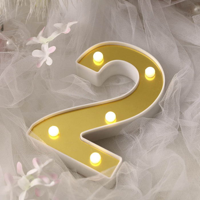 LED marquee number two with warm lights on a soft fabric backdrop.