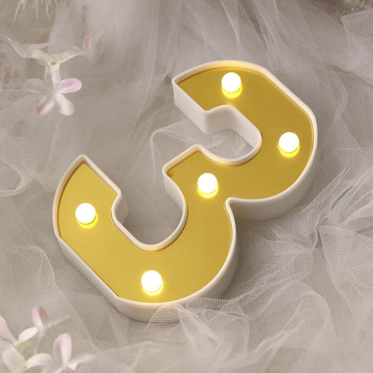 Gold LED number 3 sign on soft white fabric background.
