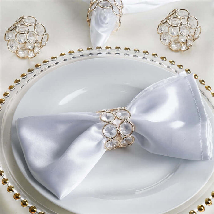 Elegant white satin napkin with crystal ring on a decorative plate.