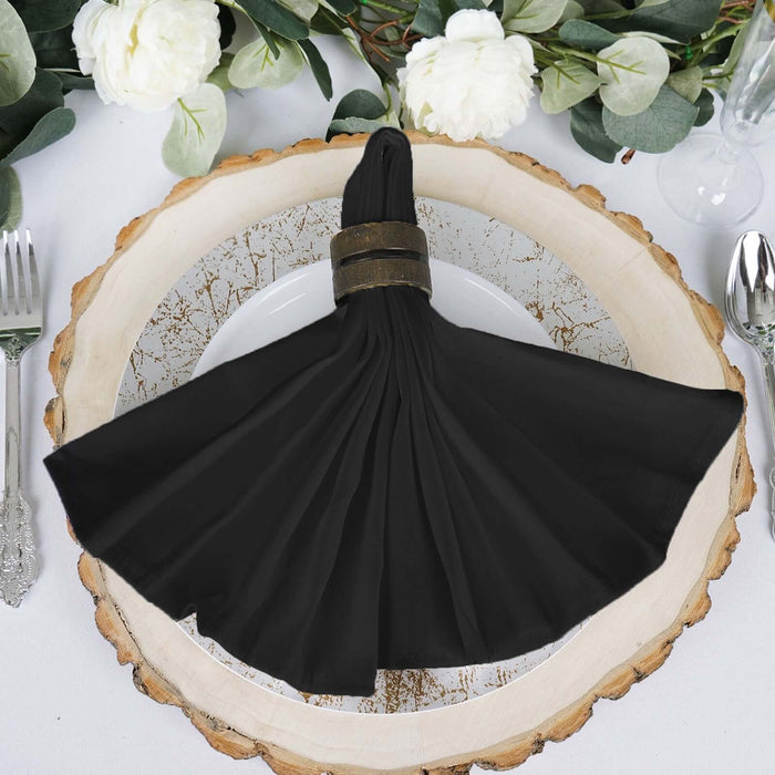 Black napkin elegantly draped on a rustic wooden plate with greenery.