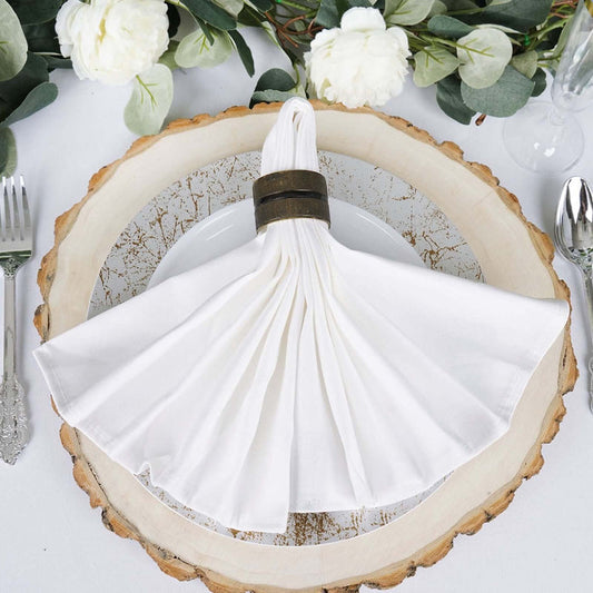 Elegant white napkin with a decorative ring on a rustic plate, surrounded by greenery.