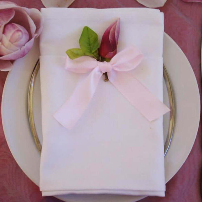Elegant white napkin with pink ribbon and floral accent on a plate.