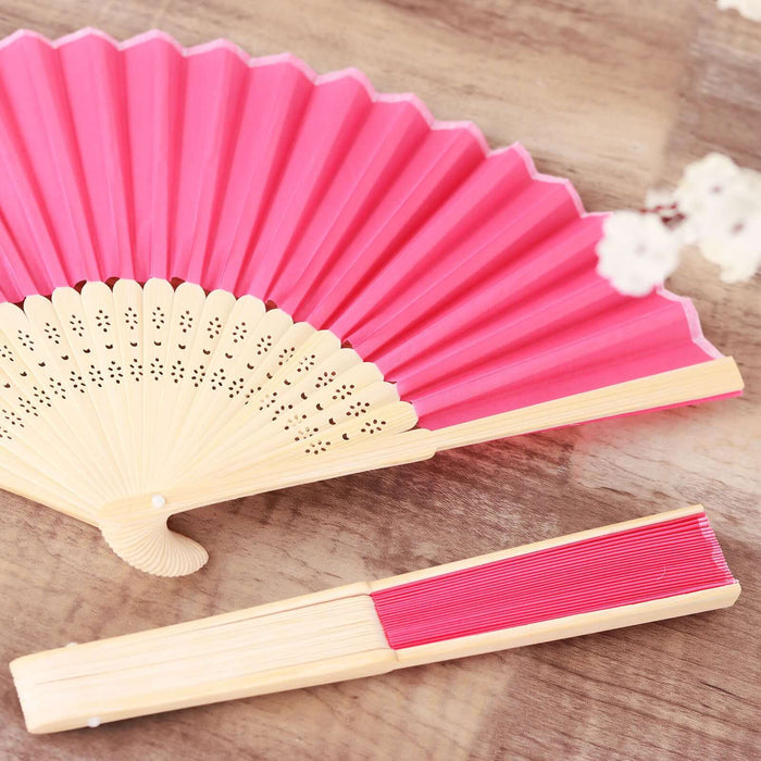 Pink decorative hand fan with intricate design on a wooden surface.