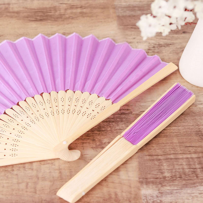 Purple folding fan and hand fan on wooden surface.