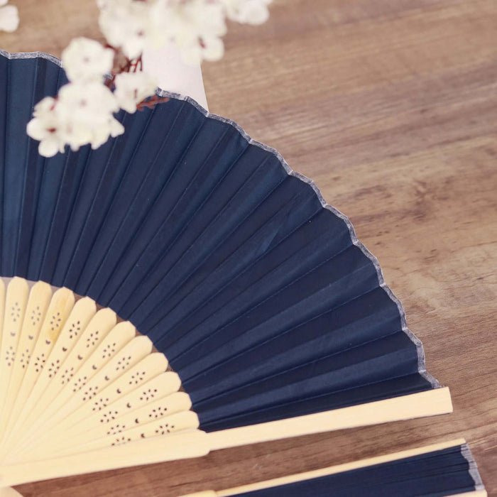 Navy blue folding fan with bamboo handle on wooden surface.