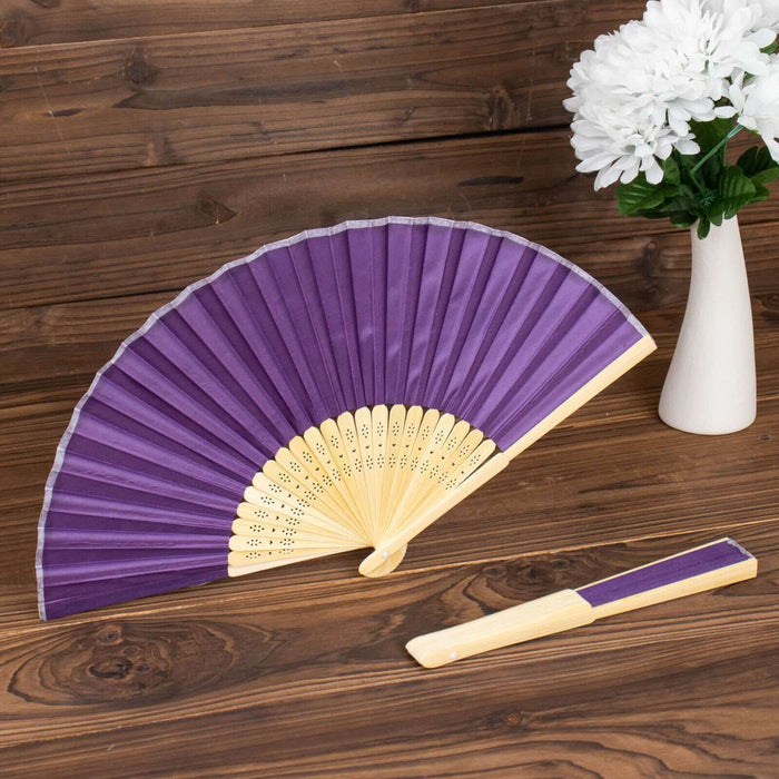 Purple folding fan with wooden handle on a wooden table.
