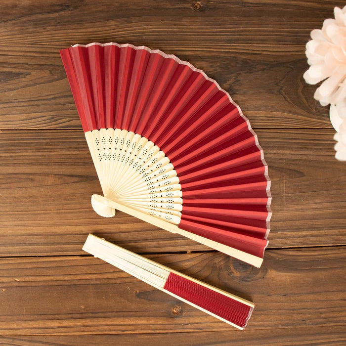 Red folding hand fan with intricate detailing on a wooden table.