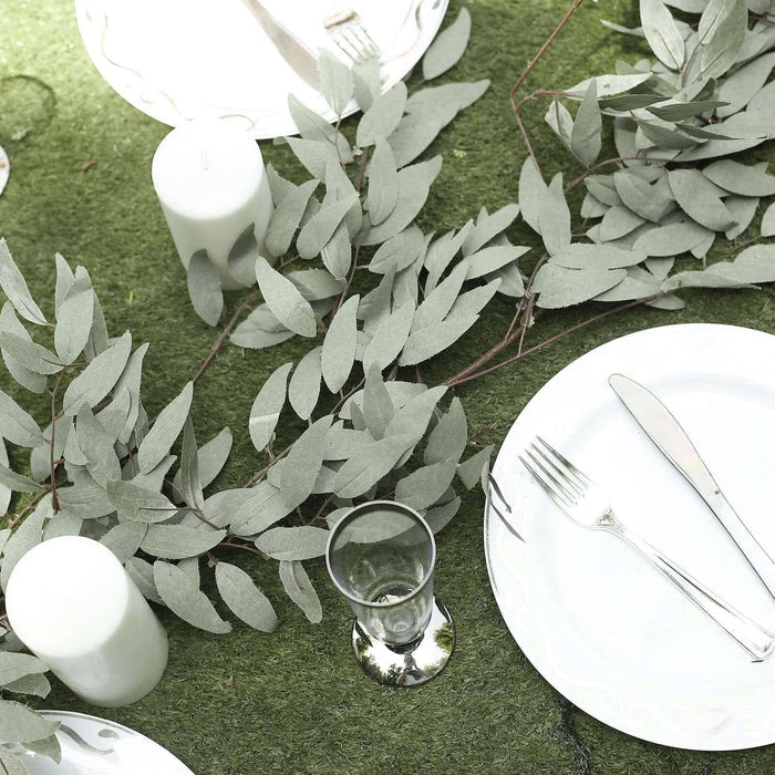 Elegant table setting with greenery and candles on a green surface.