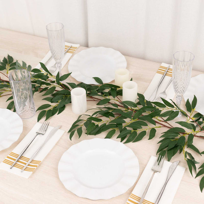 Elegant dining table set with white plates, glassware, and greenery accents.