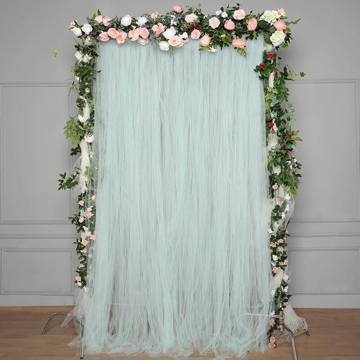 Floral backdrop with cascading mint tulle and decorative greenery for events.
