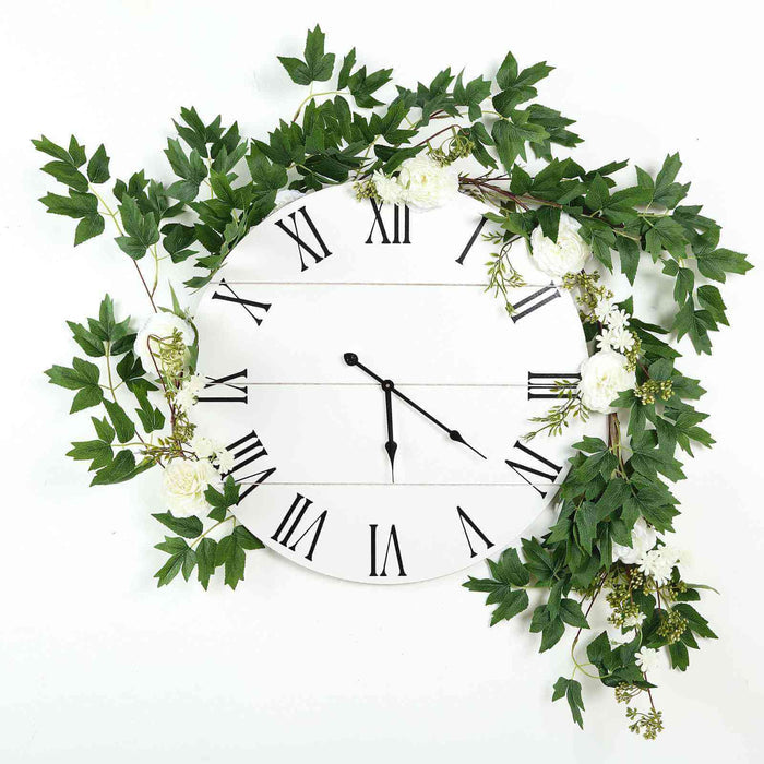 Wall clock adorned with greenery and flowers on a white background.
