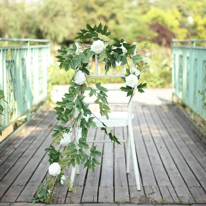 Floral garland draped over a white chair outdoors in a natural setting.
