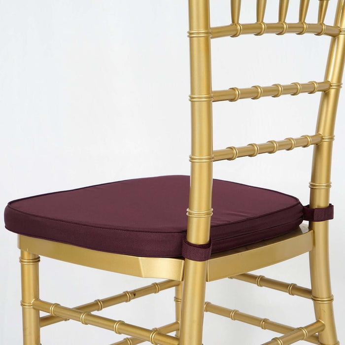 Gold chiavari chair with burgundy cushion on a plain background.