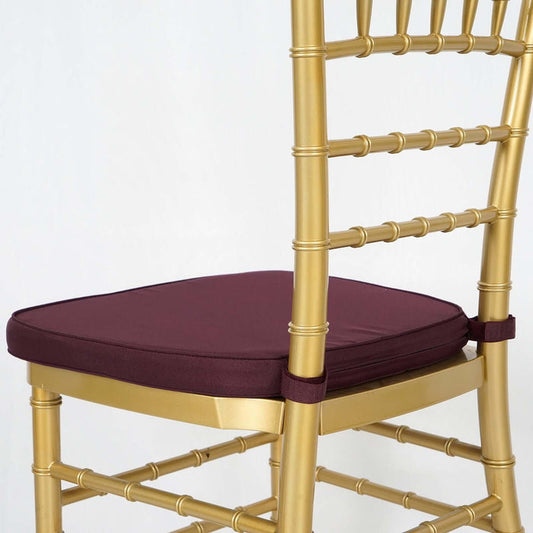 Gold chiavari chair with burgundy cushion on a plain background.