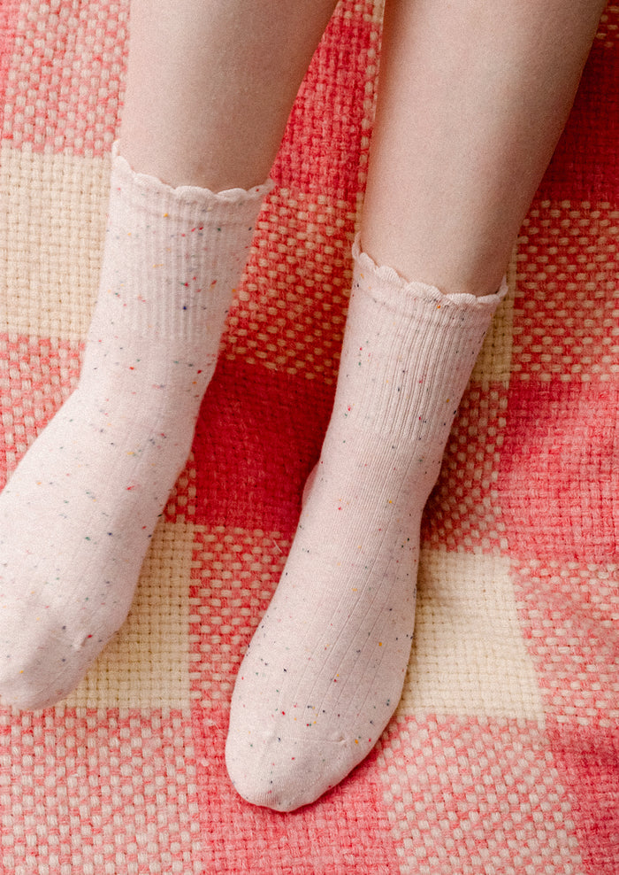 A person wearing a pair of ankle socks in light pink with multicolor speckles.