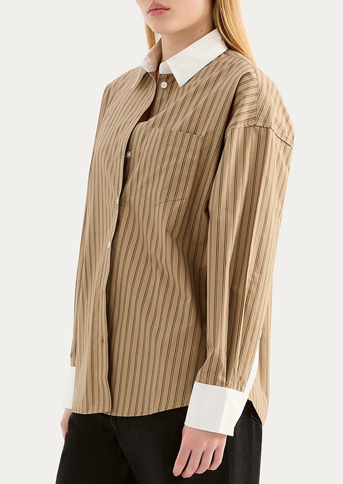A woman wearing a beige striped shirt with white collar and cuffs.
