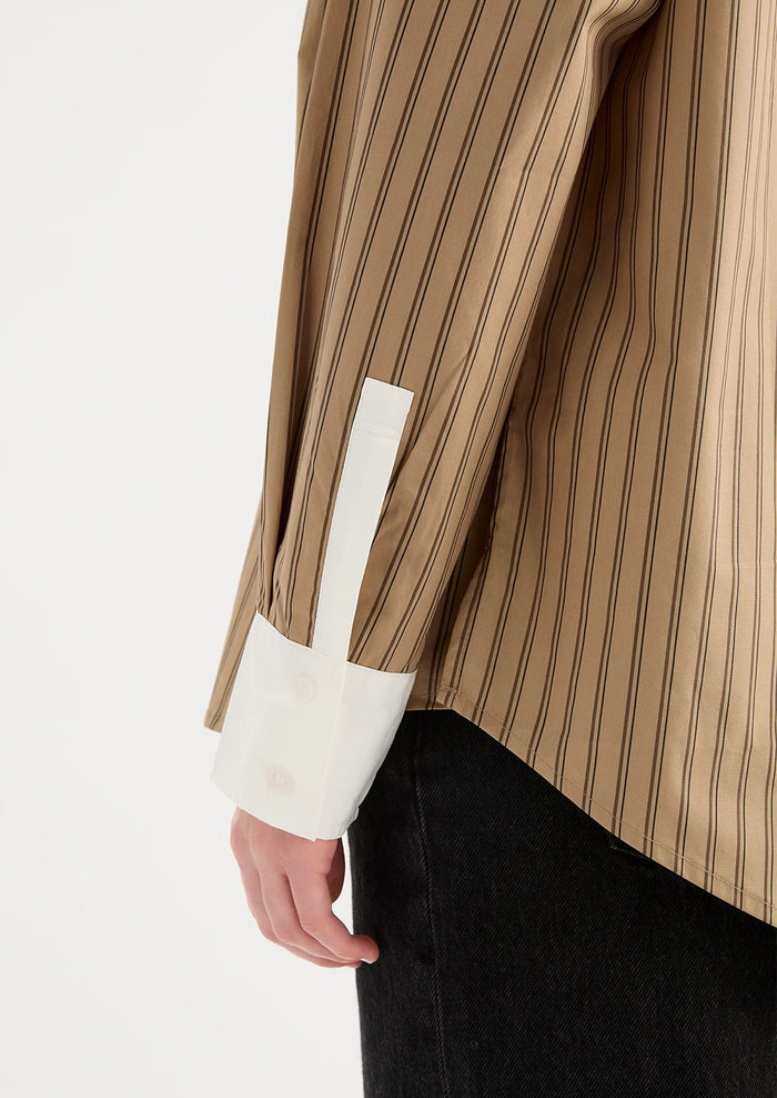 A woman wearing a beige striped shirt with white collar and cuffs.