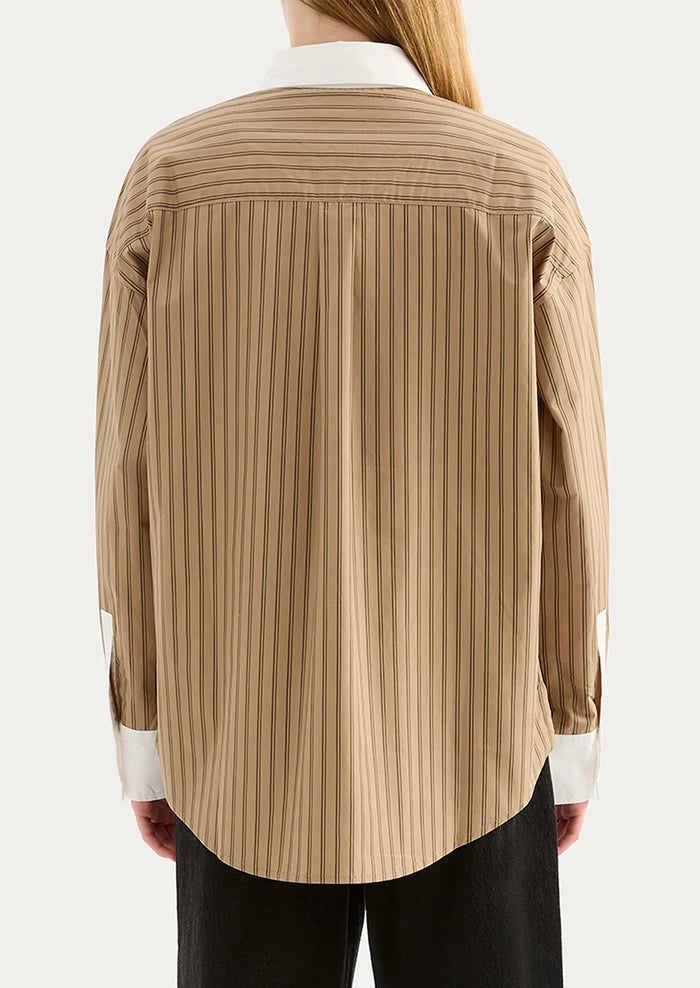 A woman wearing a beige striped shirt with white collar and cuffs.