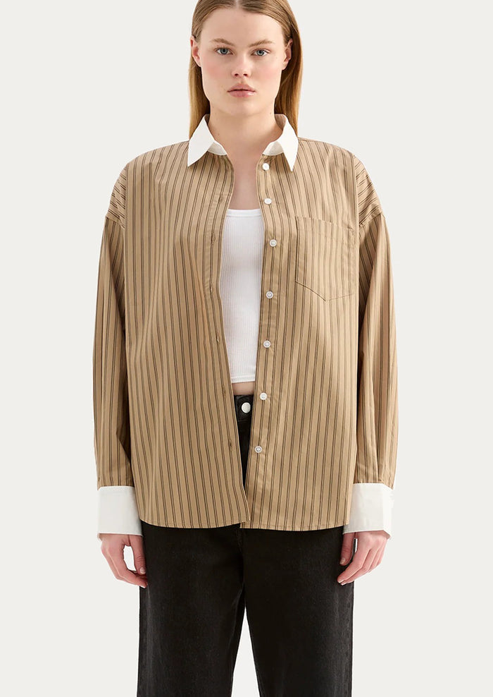 A woman wearing a beige striped shirt with white collar and cuffs.