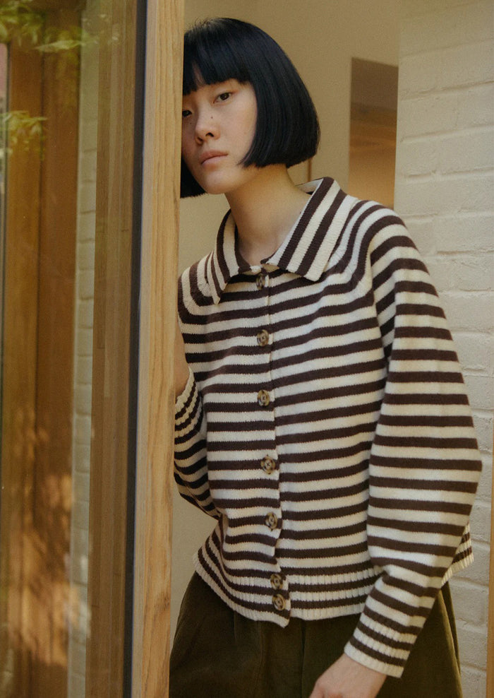 Person wearing a brown and white striped sweater in a room with wooden paneling.