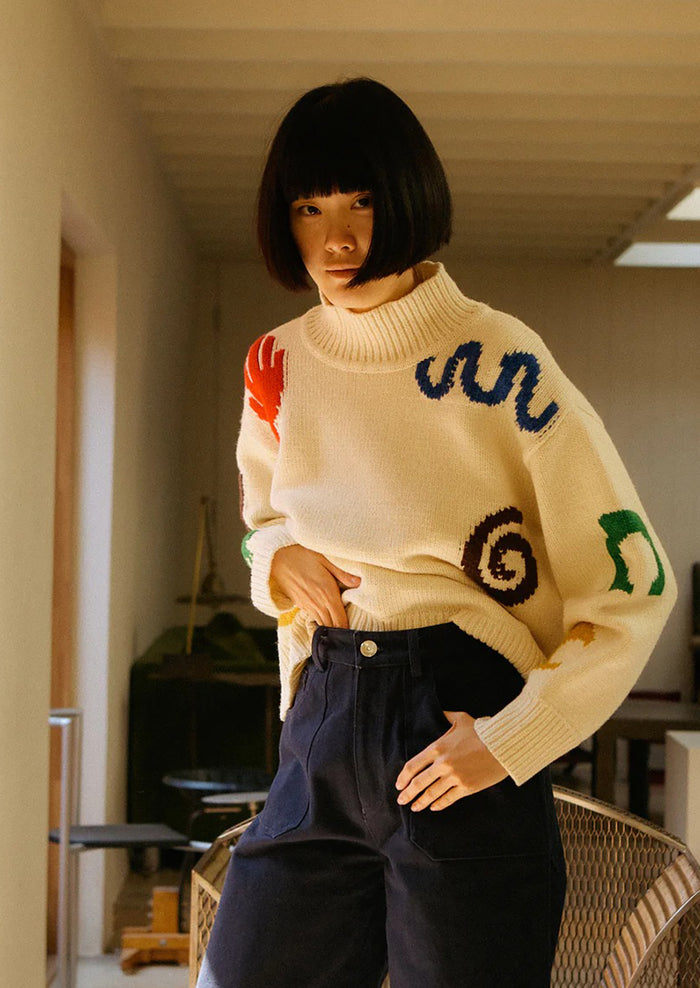 Person wearing a cream sweater with colorful patterns in an indoor setting