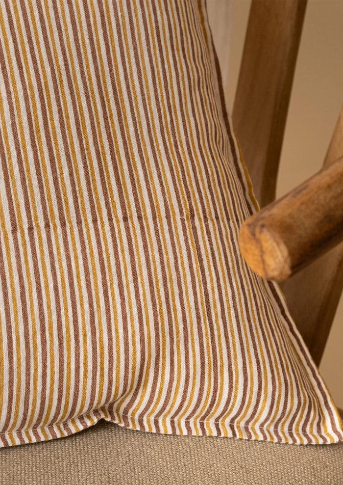 Close-up of a striped fabric cushion or pillow in warm brown, tan, and cream tones, resting against a wooden chair.
