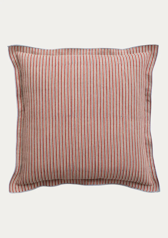A square throw pillow with vertical red and blue stripes on a beige fabric background, finished with a solid blue piped border.