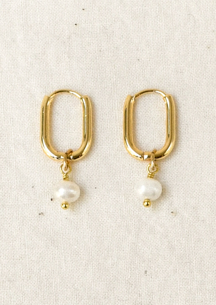 A pair of gold hoop earrings with a small white pearl dangle, displayed on a textured off-white fabric background.