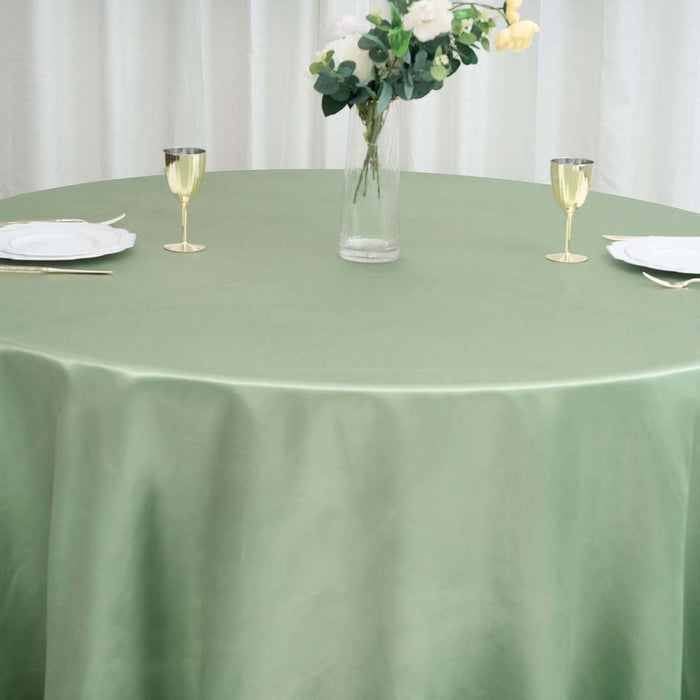 Green tablecloth draped over a round table set with glasses and floral centerpiece.