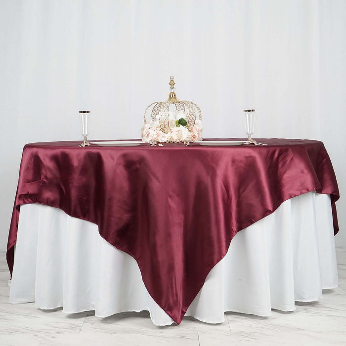 Elegant burgundy tablecloth draped over a white table with decorative crown centerpiece.
