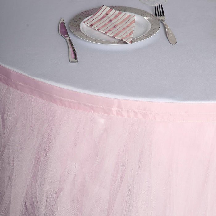 Pink tulle table skirt draped over a round table with silver plate and striped napkin.