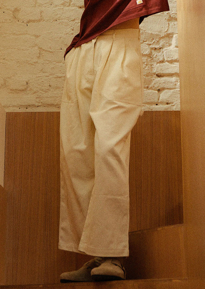 A person wearing a pair of workwear-inspired pants in ecru color.